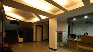 Un hall de hotel con mostrador de recepción, refrigerador, escalera y ventilador de techo.