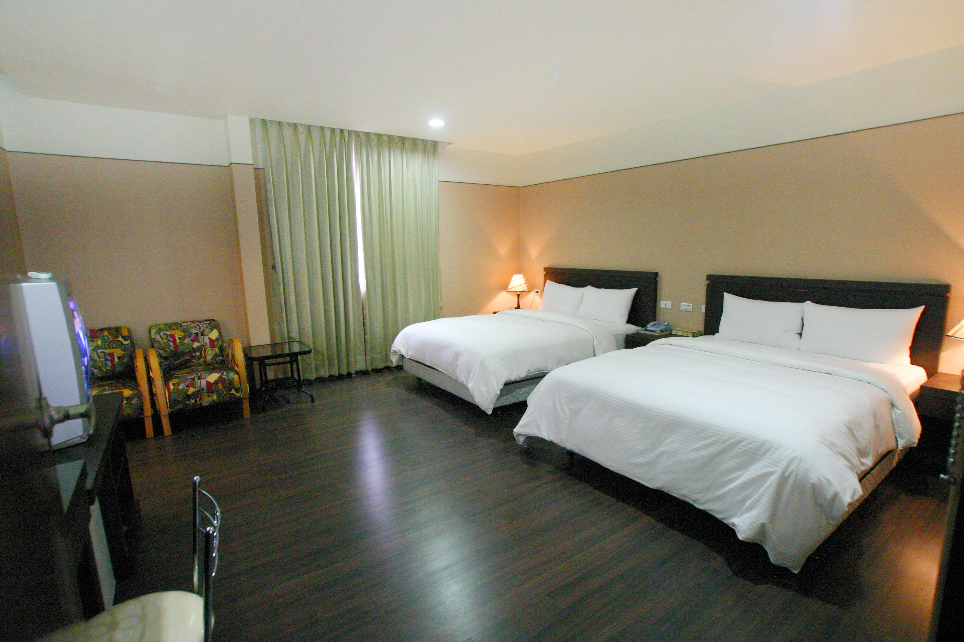 A hotel room with two beds, a desk, a chair, and a television.