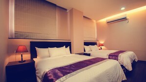 Habitación de hotel con dos camas, una mesita de noche con lámpara y un equipo de aire acondicionado en la pared.