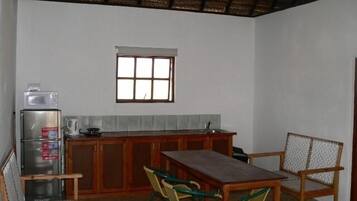 Cocina compacta con refrigerador, pileta y ventana sobre la encimera. Se ve una mesa de madera con sillas y un mueble pequeño.