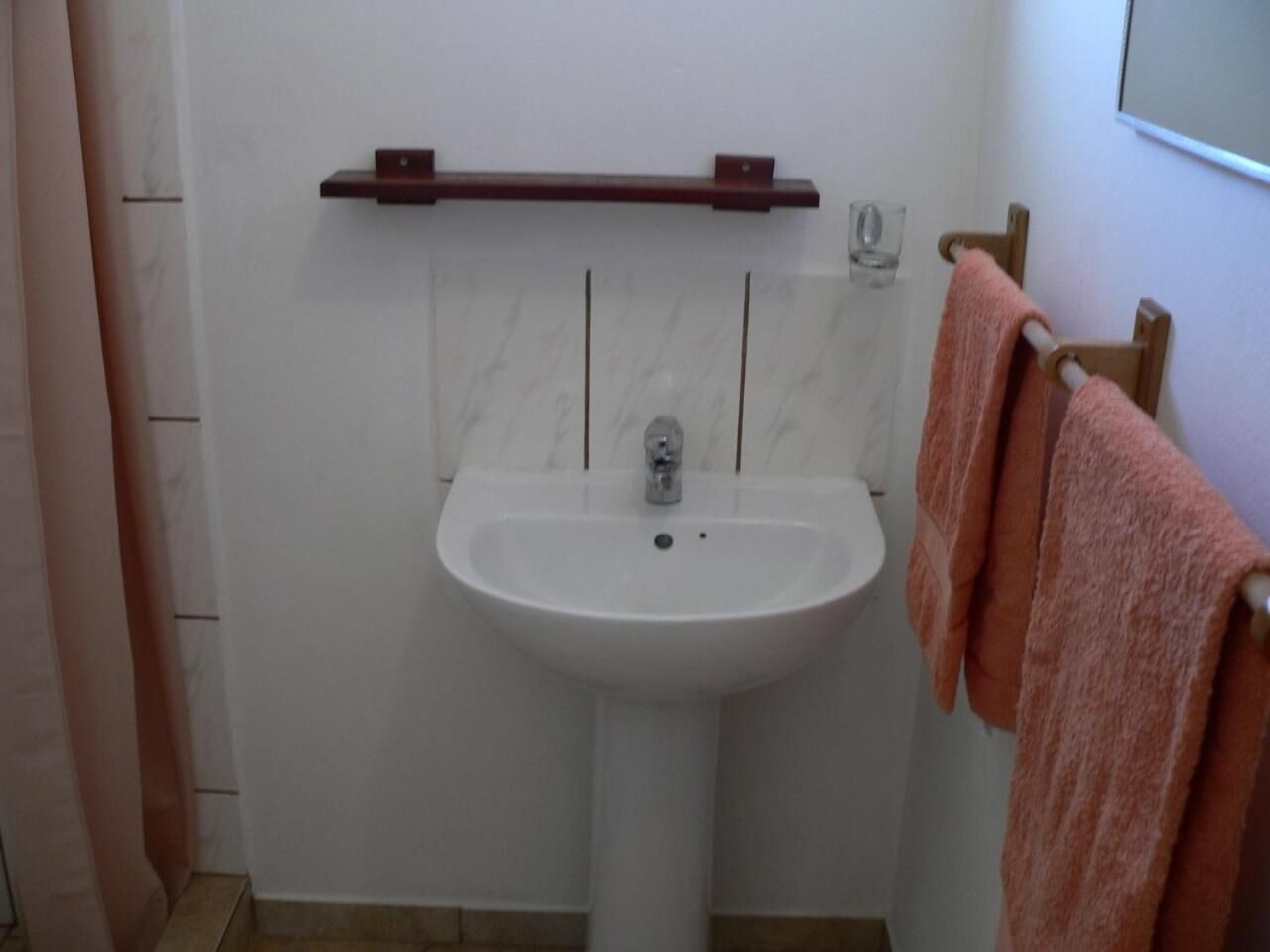 Un baño con un lavamanos blanco, un perchero de madera y un vaso en la pared.