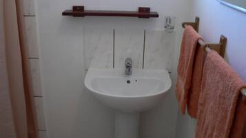 Un baño con un lavamanos blanco, un perchero de madera y un vaso en la pared.