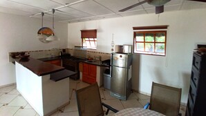 A compact kitchen with a central island, a refrigerator, and a ceiling fan. - Blue Moon Beach Holiday Resort (Jangamo)