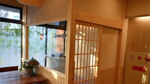 Una habitación tradicional japonesa con suelo de tatami, una mesa de madera con sillas, una puerta corredera de shoji y un pequeño equipo de aire acondicionado en la pared.