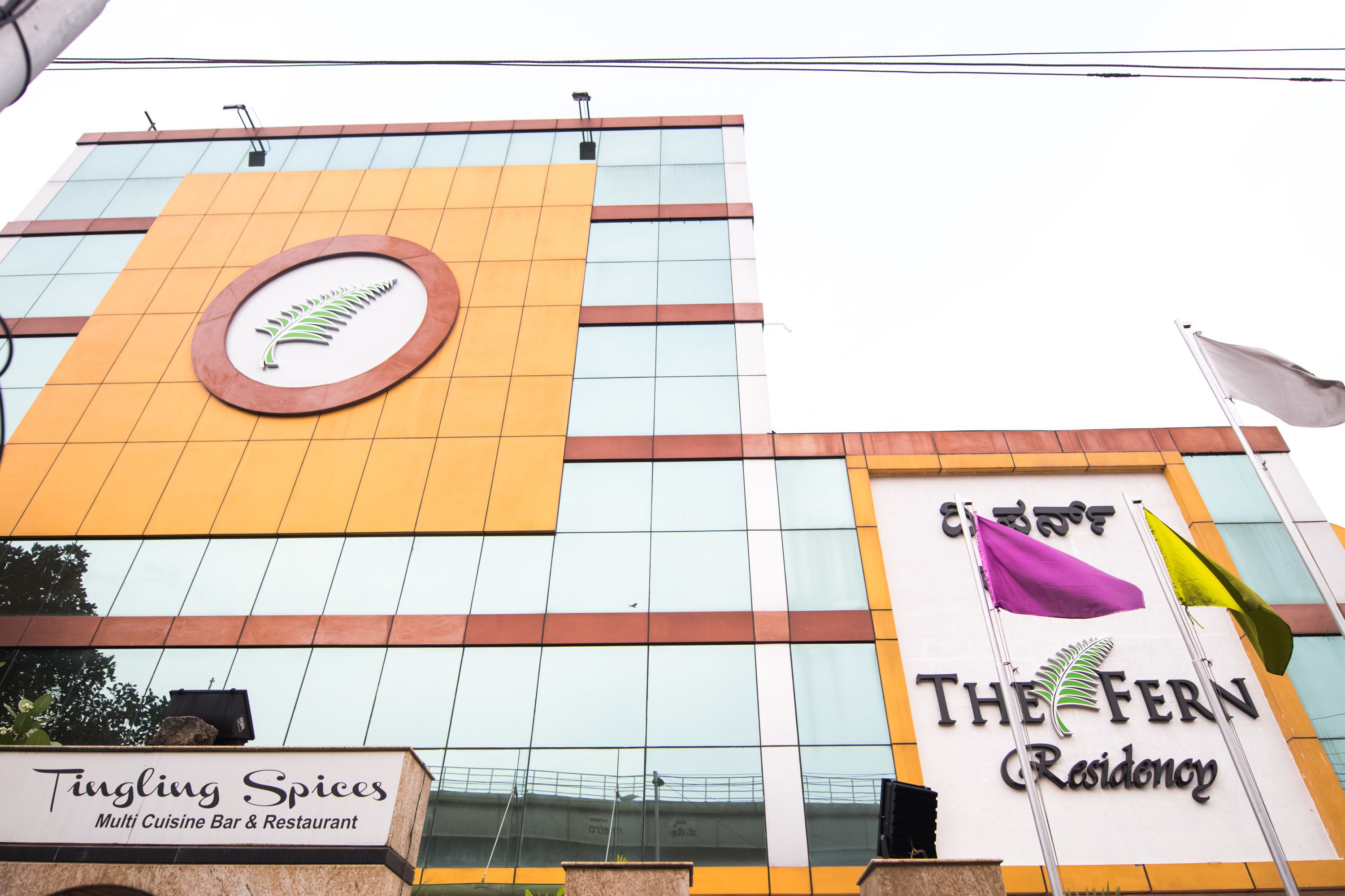 A building with a sign for Tingling Spices Multi Cuisine Bar & Restaurant and The Fern Residency.