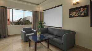 A modern living room with a grey sofa, a small table with a plant, and a large window offering a city view. - The Fern Residency Bengaluru, Yeshwanthpur, Series by Marriott (Bengaluru)