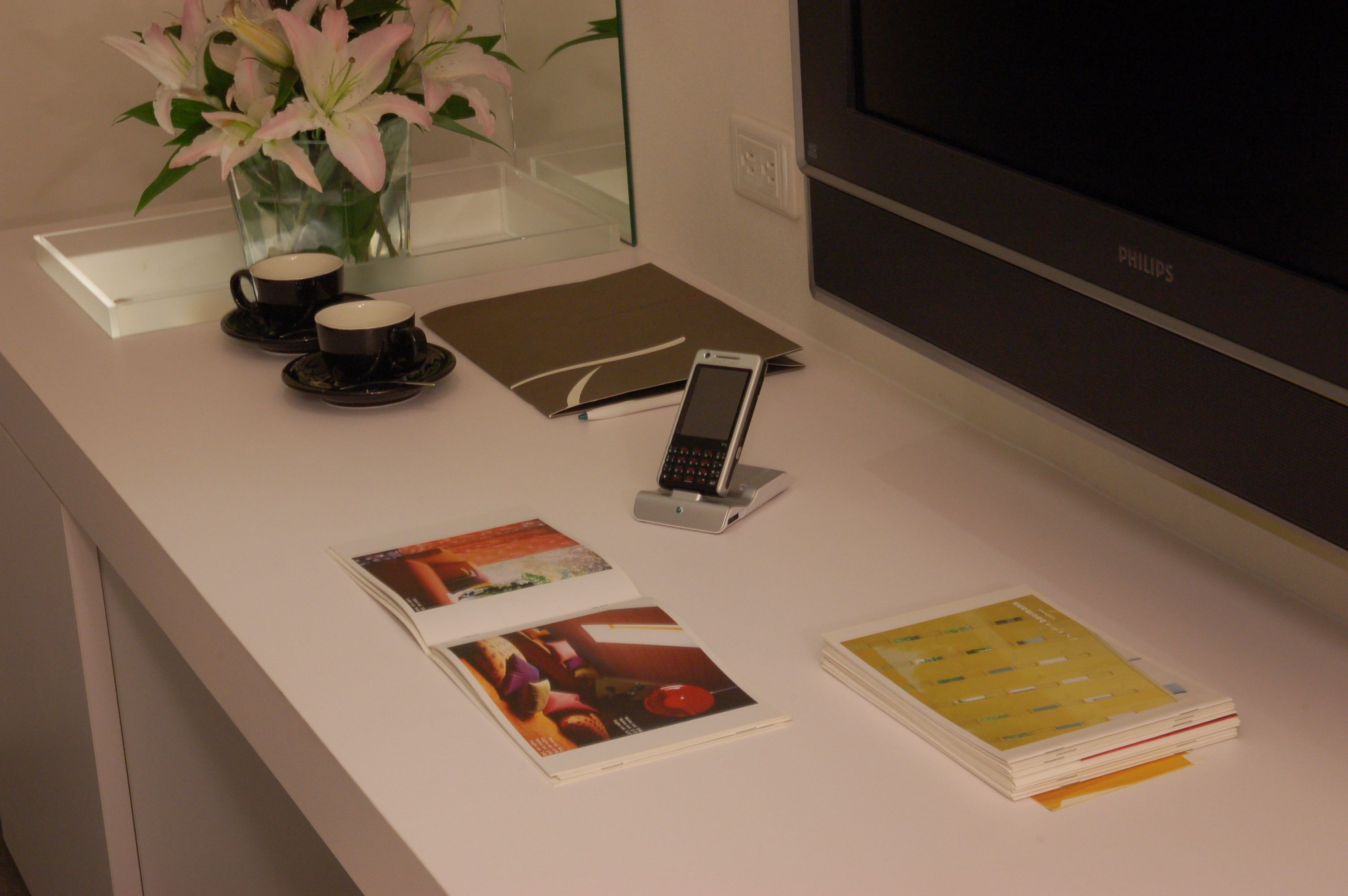 A clean desk with a laptop, a smartphone, a cup, a vase with flowers, and a magazine.