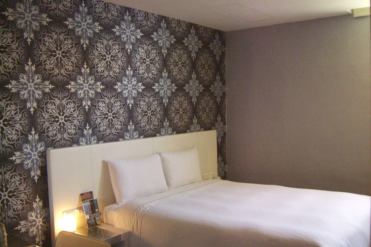 A hotel room with a bed, a nightstand, and a table.