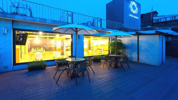 Un hotel con terraza al aire libre, fachada de vidrio y un logotipo destacado en el edificio.