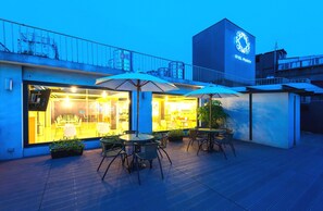 A hotel with outdoor seating, a glass facade, and a prominent logo on the building. - Hotel Purity (New Taipei City)