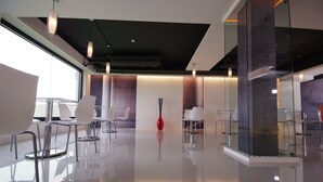 Una sala de conferencias moderna y bien iluminada, con piso brillante, sillas blancas y un jarrón rojo en el centro.