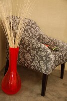 Un vase rouge avec des baguettes blanches, un fauteuil à motifs et un livre posé dessus.