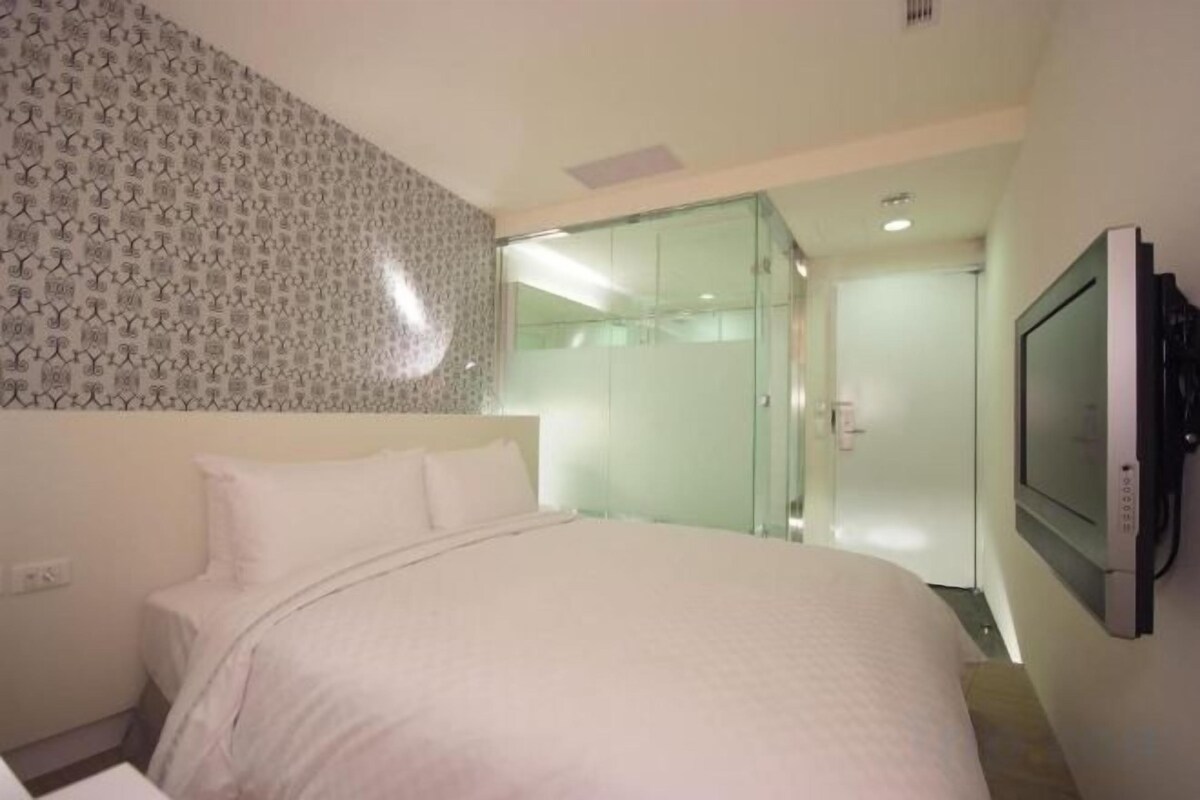 A hotel room with a bed, a television, and a glass shower enclosure.