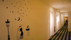 Un pasillo de hotel con adhesivos de estrellas y luna en la pared, una lámpara e ilustración de un gato.