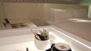 Una habitación de hotel con una cama bien hecha, una mesita de noche con una taza de café y un mando a distancia, y un papel tapiz estampado en la pared.