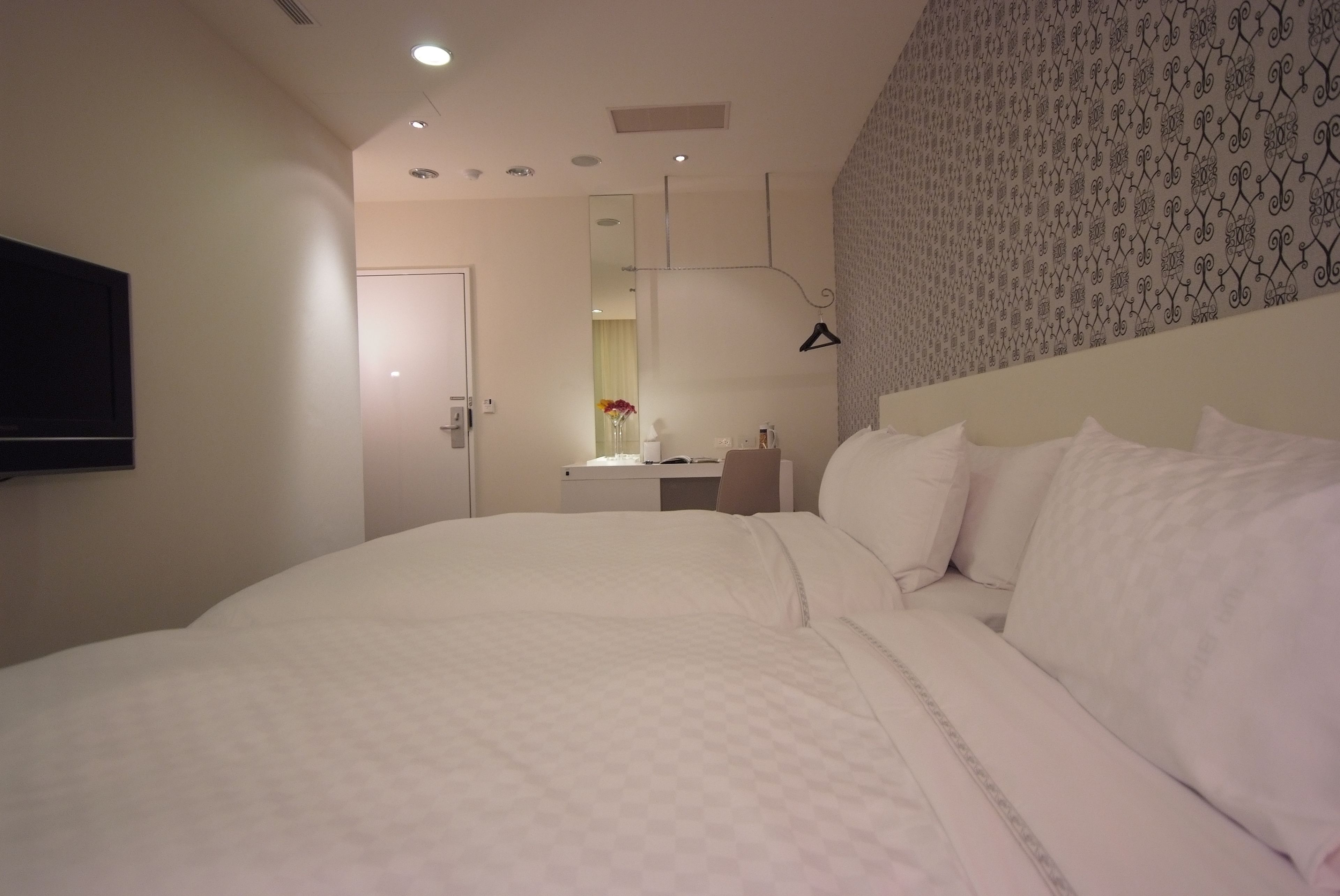 A hotel room with a large bed, a desk with a chair, a mirror, and a television mounted on the wall.