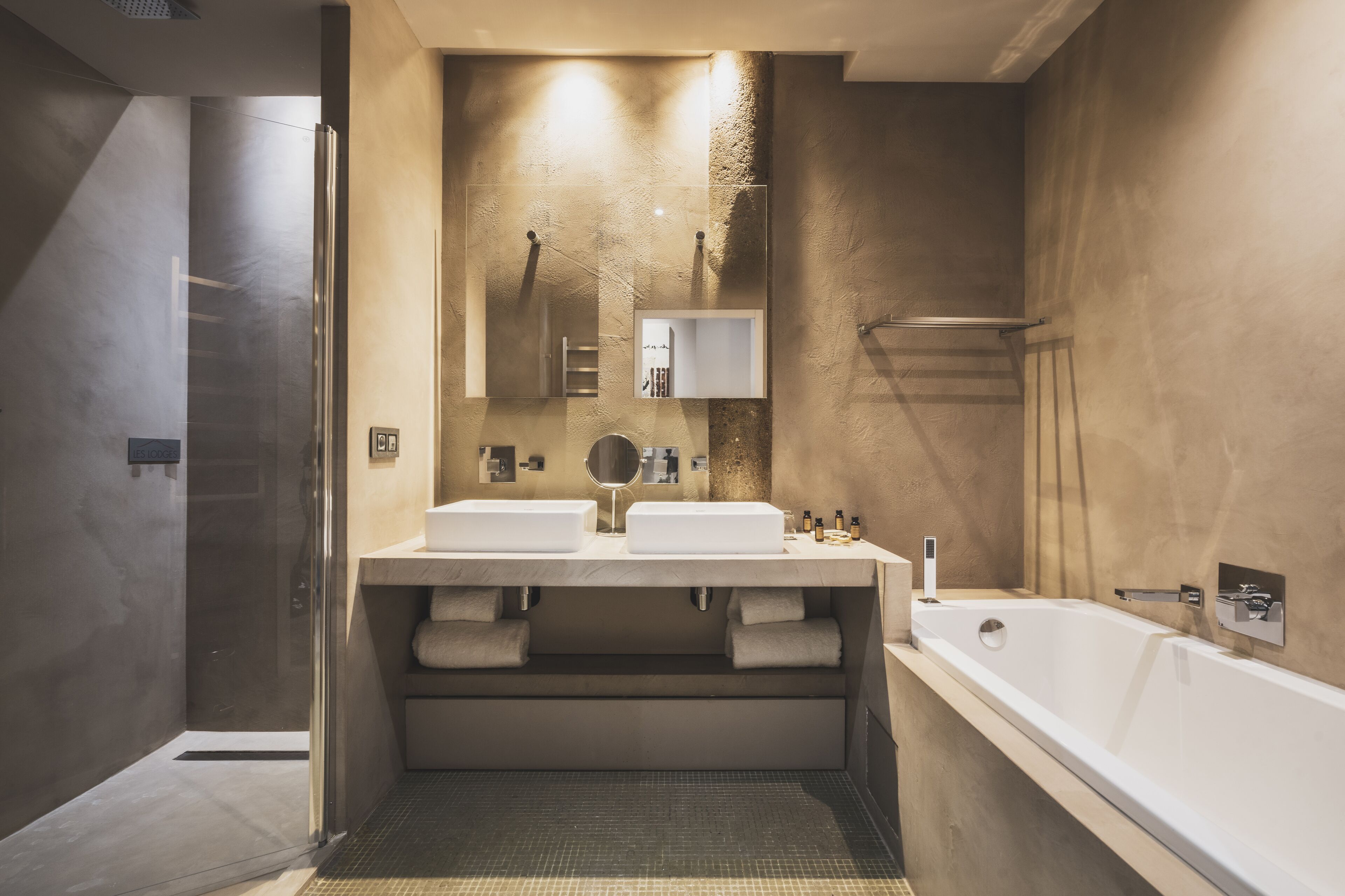 Ein modernes Badezimmer mit zwei Waschbecken, einem großen Spiegel, einer Badewanne und einer Duschkabine aus Glas.