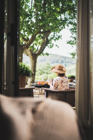 A person seated at a table with a view of a tree and landscape.