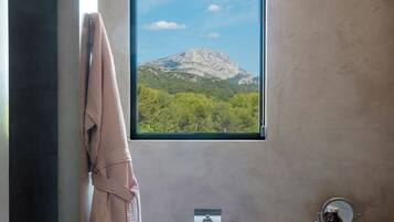 Un baño con bañera, una ventana con vista a la montaña, un perchero para toallas y un espejo.