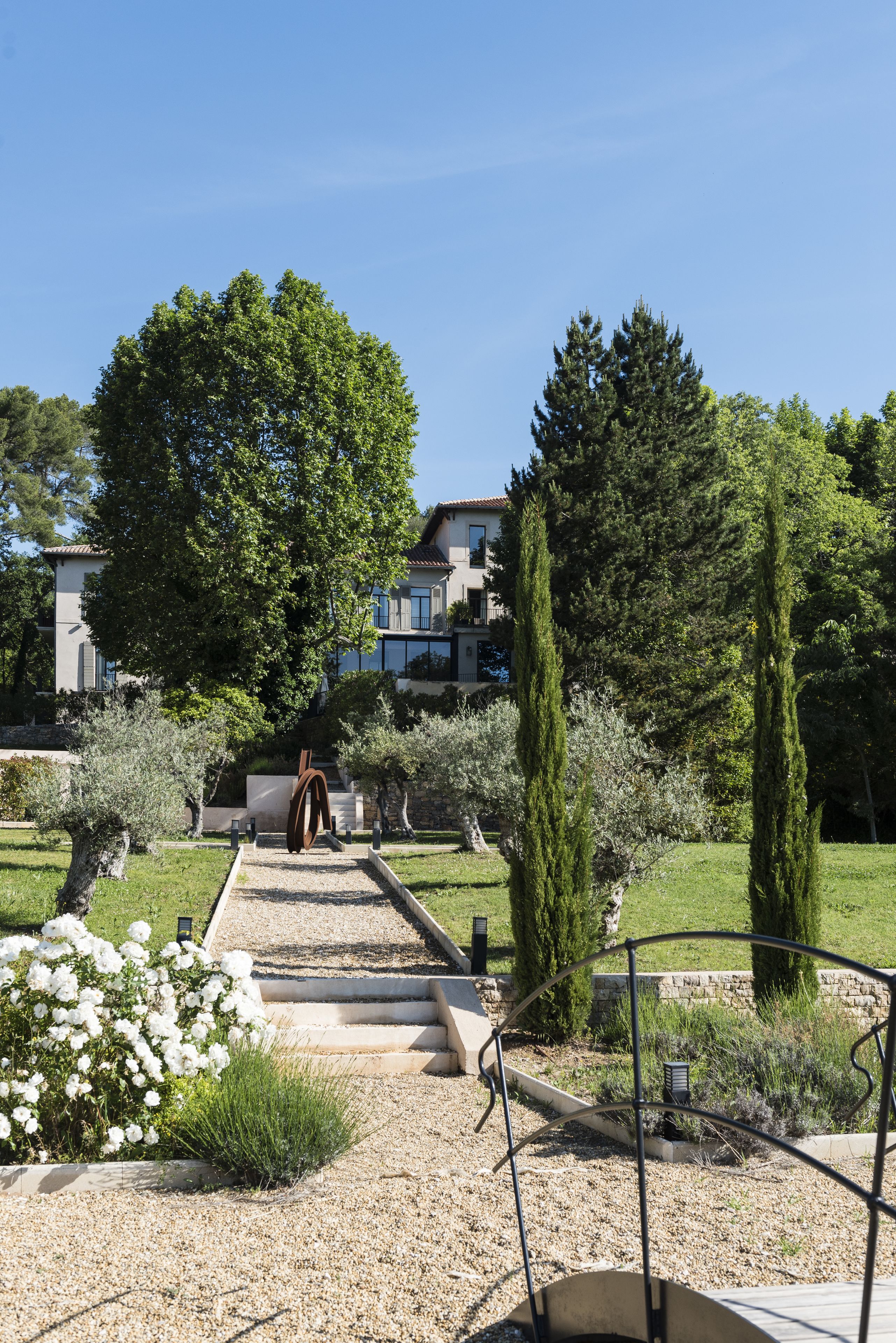 Un chemin de jardin menant à un bâtiment à l’architecture moderne, entouré de différentes plantes et de divers arbres.