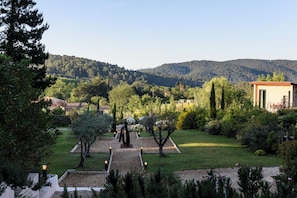 A garden with a pathway leading to a building, surrounded by trees and hills.