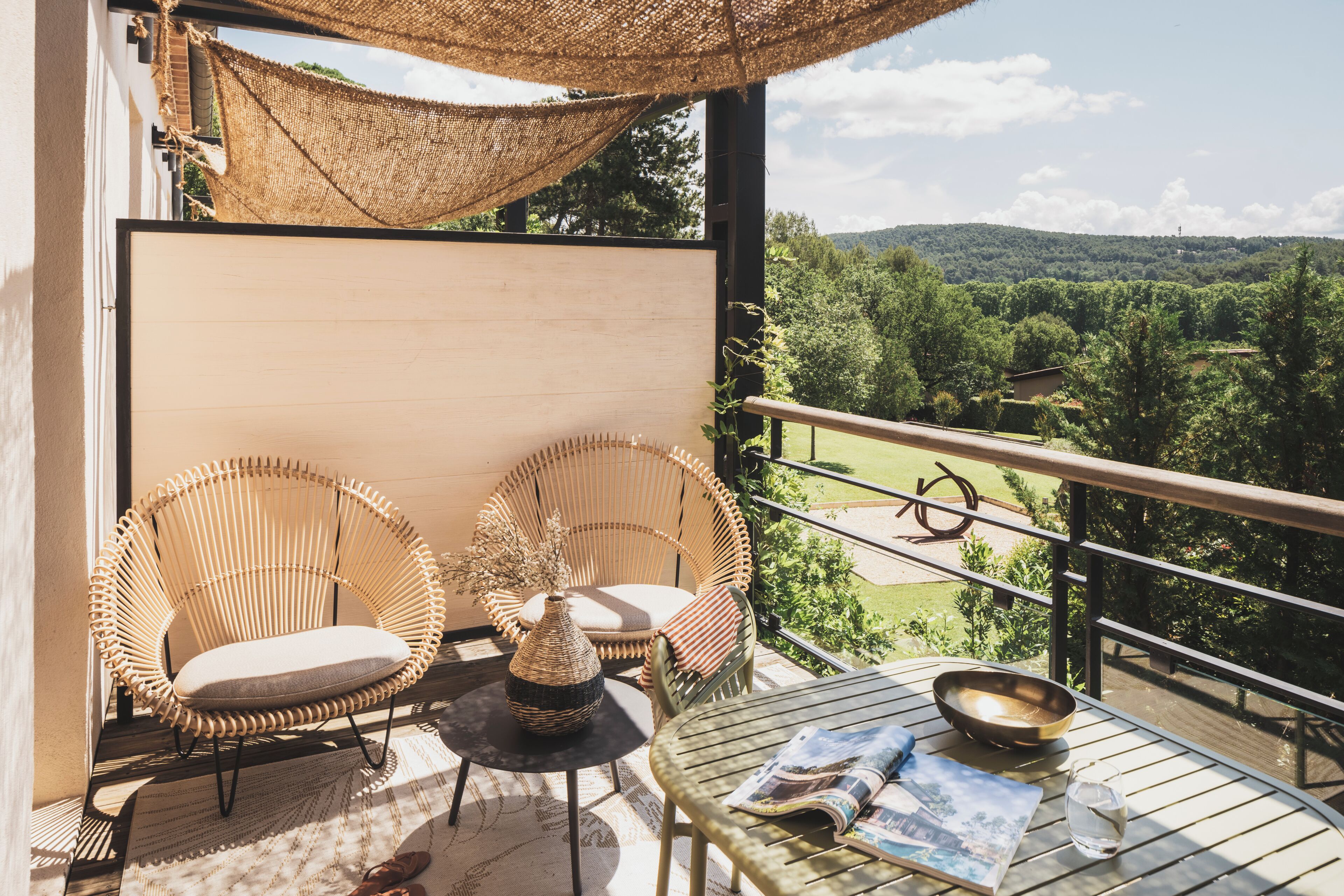 A balcony with wicker chairs, a table, a vase, and a bowl.