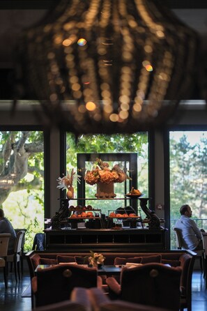 A restaurant with a central display of food, a chandelier, and large windows with a view of greenery. - Les Lodges Sainte-Victoire Hotel & Spa (Le Tholonet)