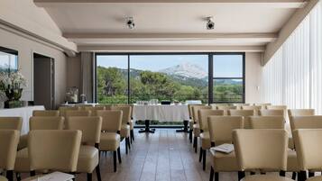 Un salón de conferencias con vistas a la montaña, sillas dispuestas y una mesa con mantel blanco.