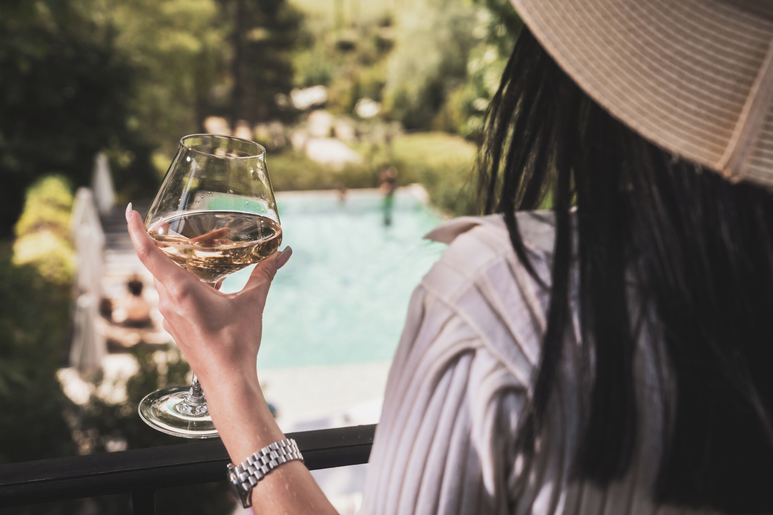 Una persona sosteniendo una copa de vino, con vista a una piscina y un paisaje verde exuberante al fondo.