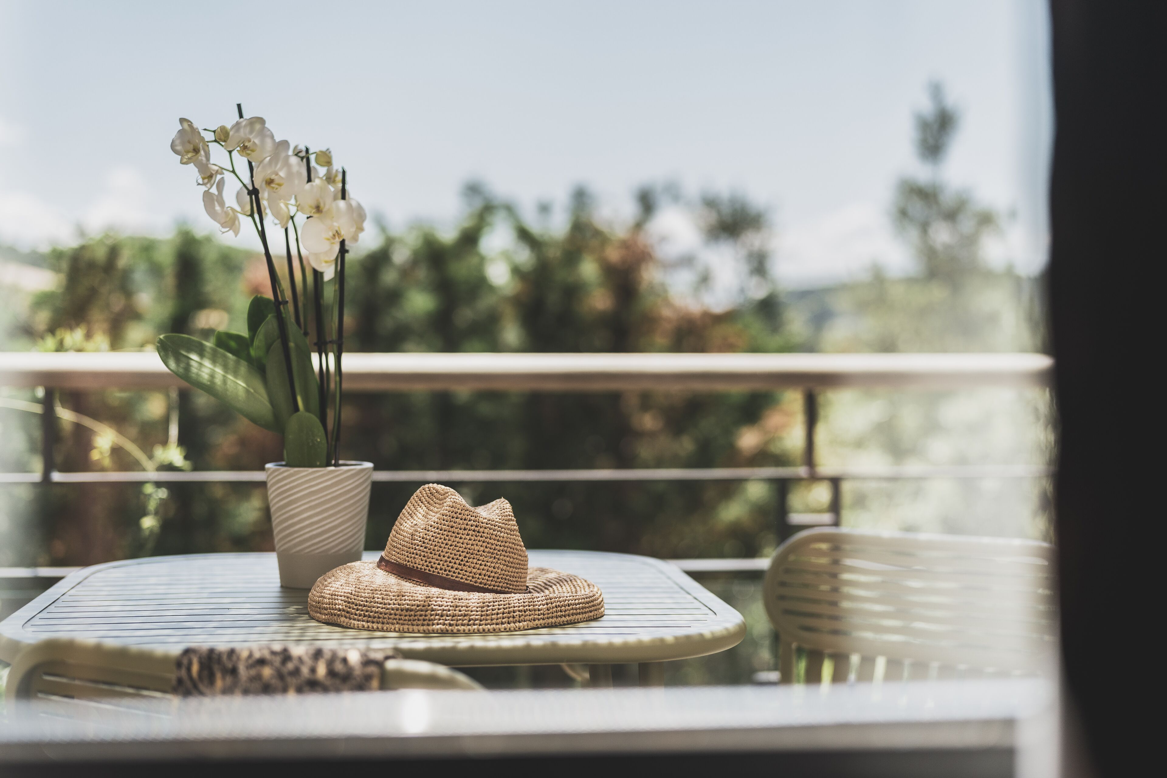 A round table with a woven hat and a potted orchid.