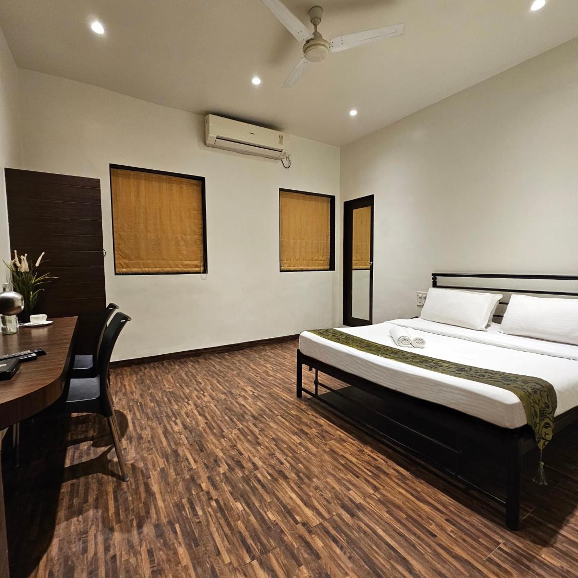 A hotel room with a bed, a desk, chairs, an air conditioning unit, and a ceiling fan.