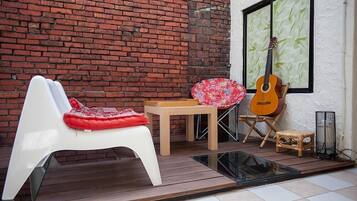 Un patio con una silla blanca, una pequeña mesa, una guitarra y un taburete de mimbre.