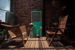 A wooden deck with wicker chairs and a wooden table, a green door, and a brick wall. - May Rooms Taipei - Nangang Station (Taipei)