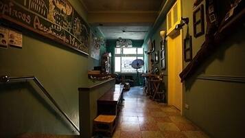 Un pasillo estrecho con una escalera a la izquierda, un mostrador con un ventilador a la derecha y un mural en la pared.