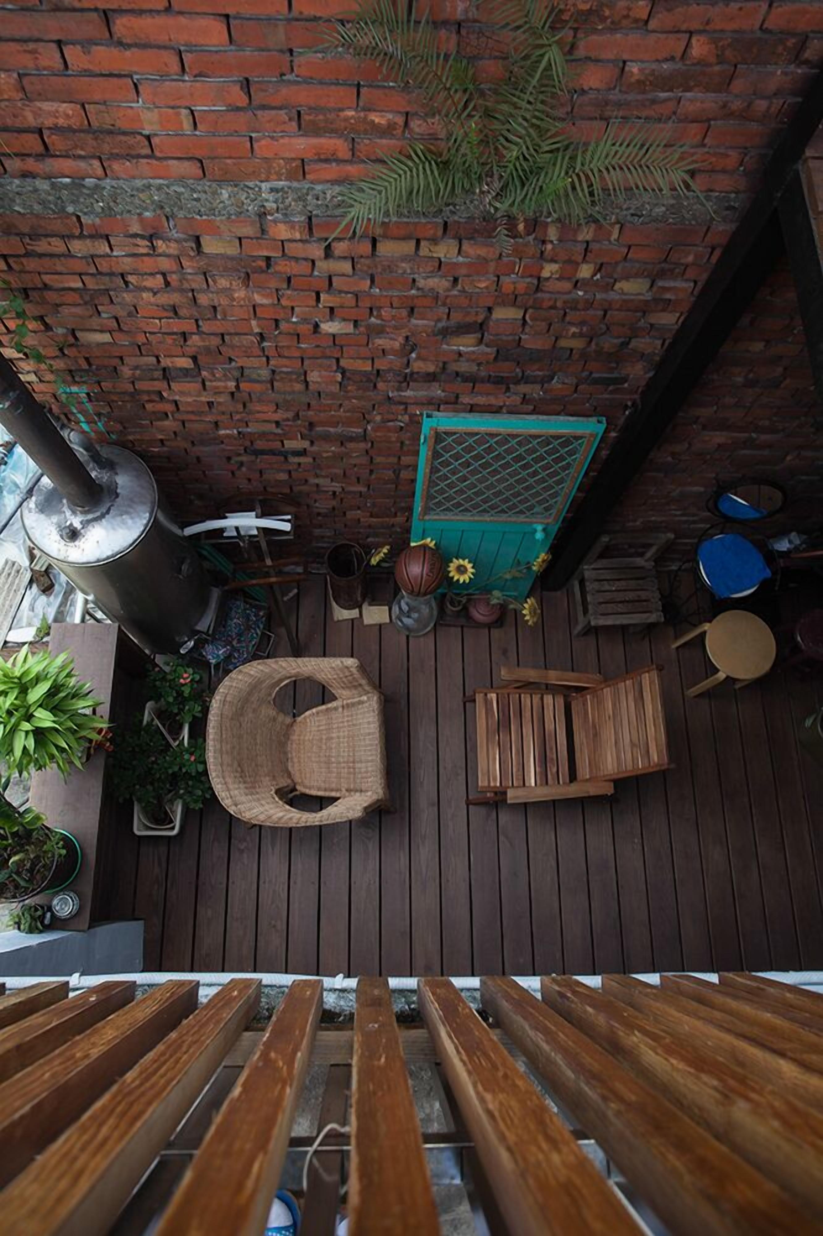 Una terraza de madera con un muro de ladrillo, un calentador metálico y varios maceteros con plantas.