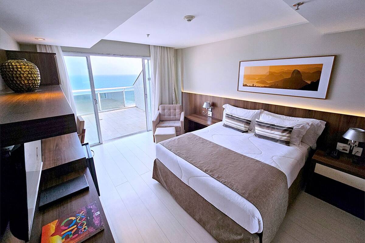 A modern hotel room with a large bed, a desk, a chair, and a view of the ocean.