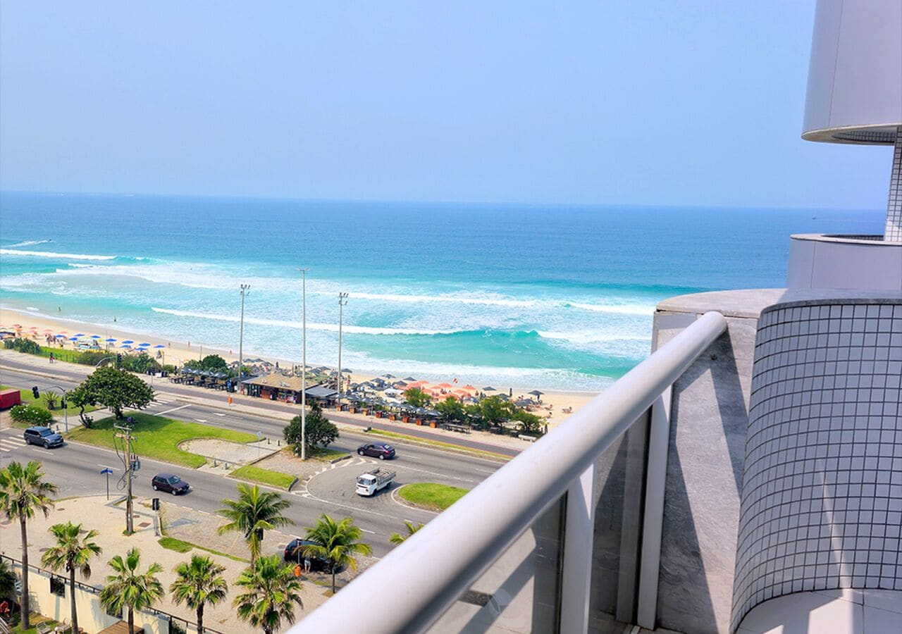 A coastal view from a balcony overlooking a beach with a road and palm trees.