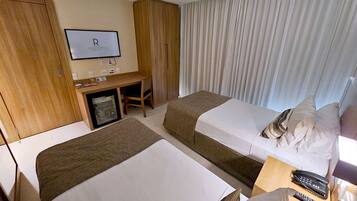 Habitación de hotel con dos camas, un escritorio con computadora, un televisor en la pared y una ventana con cortinas.