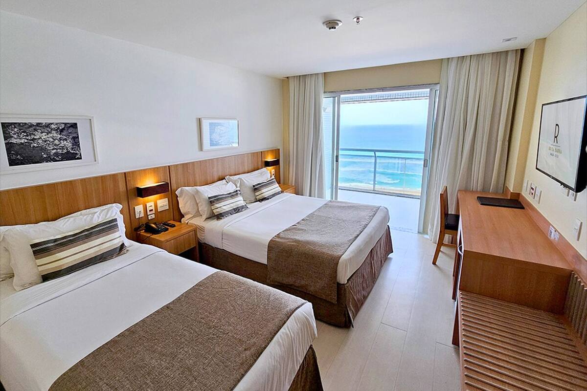 A hotel room with two beds, a desk, and a view of the ocean.