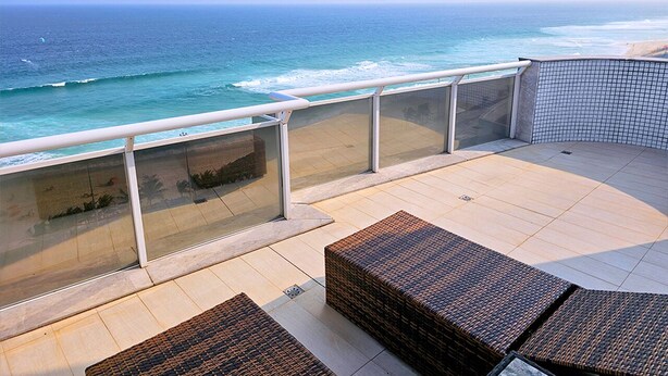 A balcony with wicker furniture and glass railings overlooking the ocean.