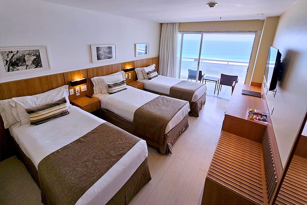 A hotel room with three beds, a desk, and a TV.