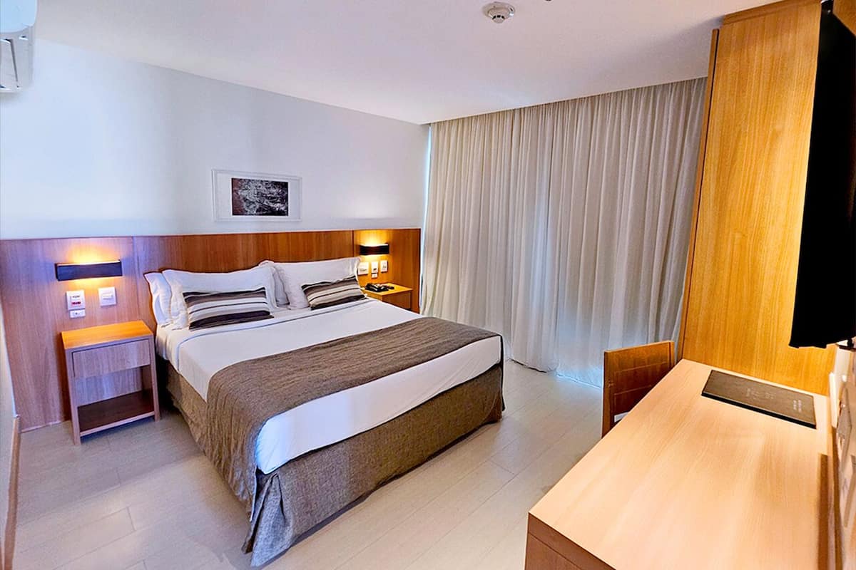 A hotel room with a large bed, bedside tables, a desk, and a window with curtains.