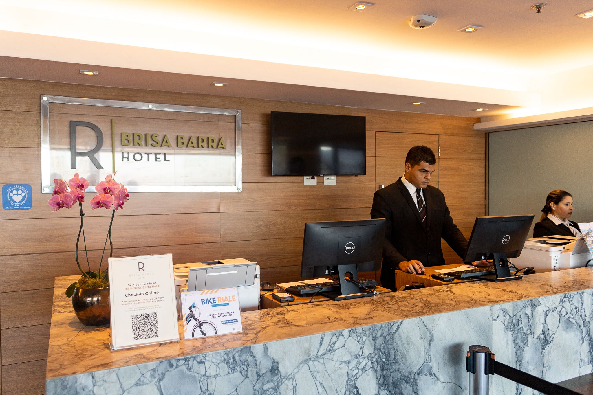 Ein Hotelrezeptionstresen mit einem Schild mit der Aufschrift 'BRISA BARRA HOTEL' und einem digitalen Bildschirm darüber.