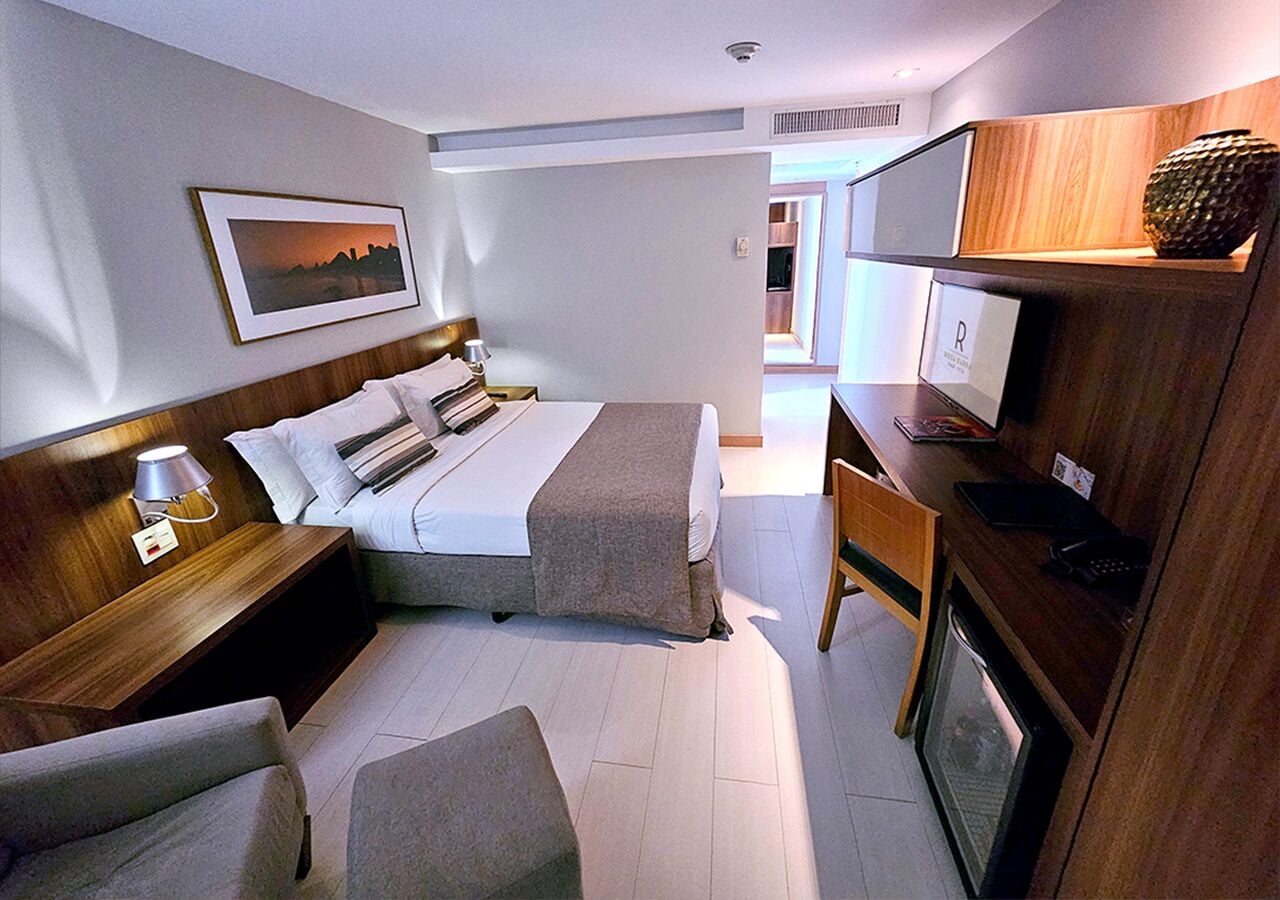 A hotel room with a bed, two bedside tables, a desk, a chair, and a television.