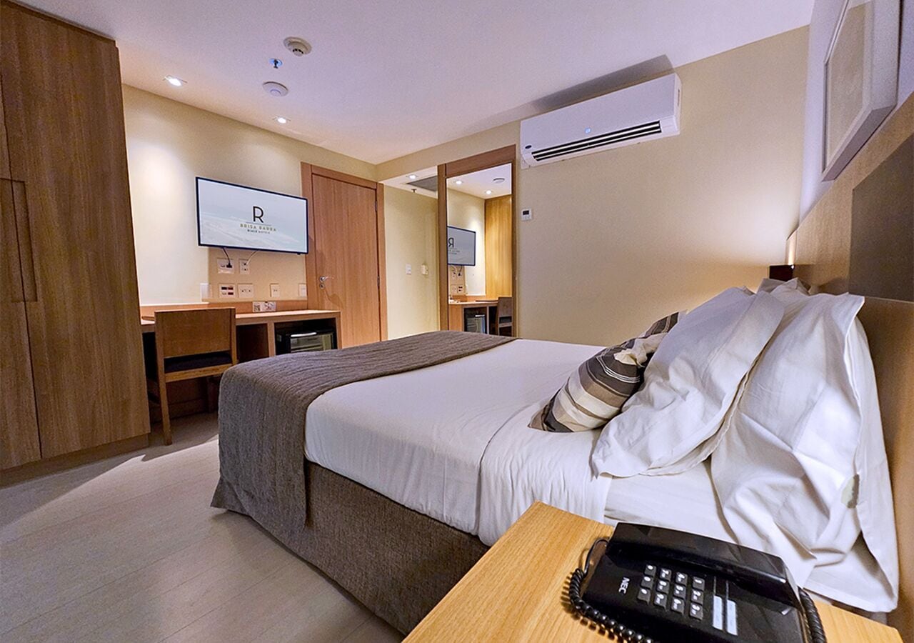Ein Hotelzimmer mit Bett, Schreibtisch, Stuhl, Fernseher und Klimaanlage.