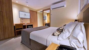 Ein Hotelzimmer mit Bett, Schreibtisch, Stuhl, Fernseher und Klimaanlage.