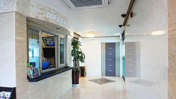A hotel lobby with a reception desk, a potted plant, and a door leading to another room. - Hotel Maple (Jeju City)