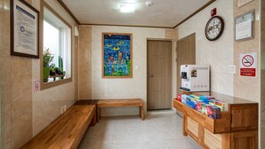 A hallway with a wooden bench, a clock, a vending machine, and a painting on the wall. - Hotel Maple (Jeju City)