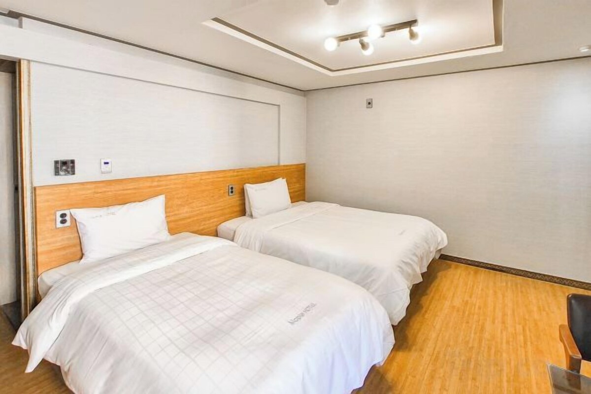A hotel room with two single beds, a wooden headboard, a small desk, and a chair.