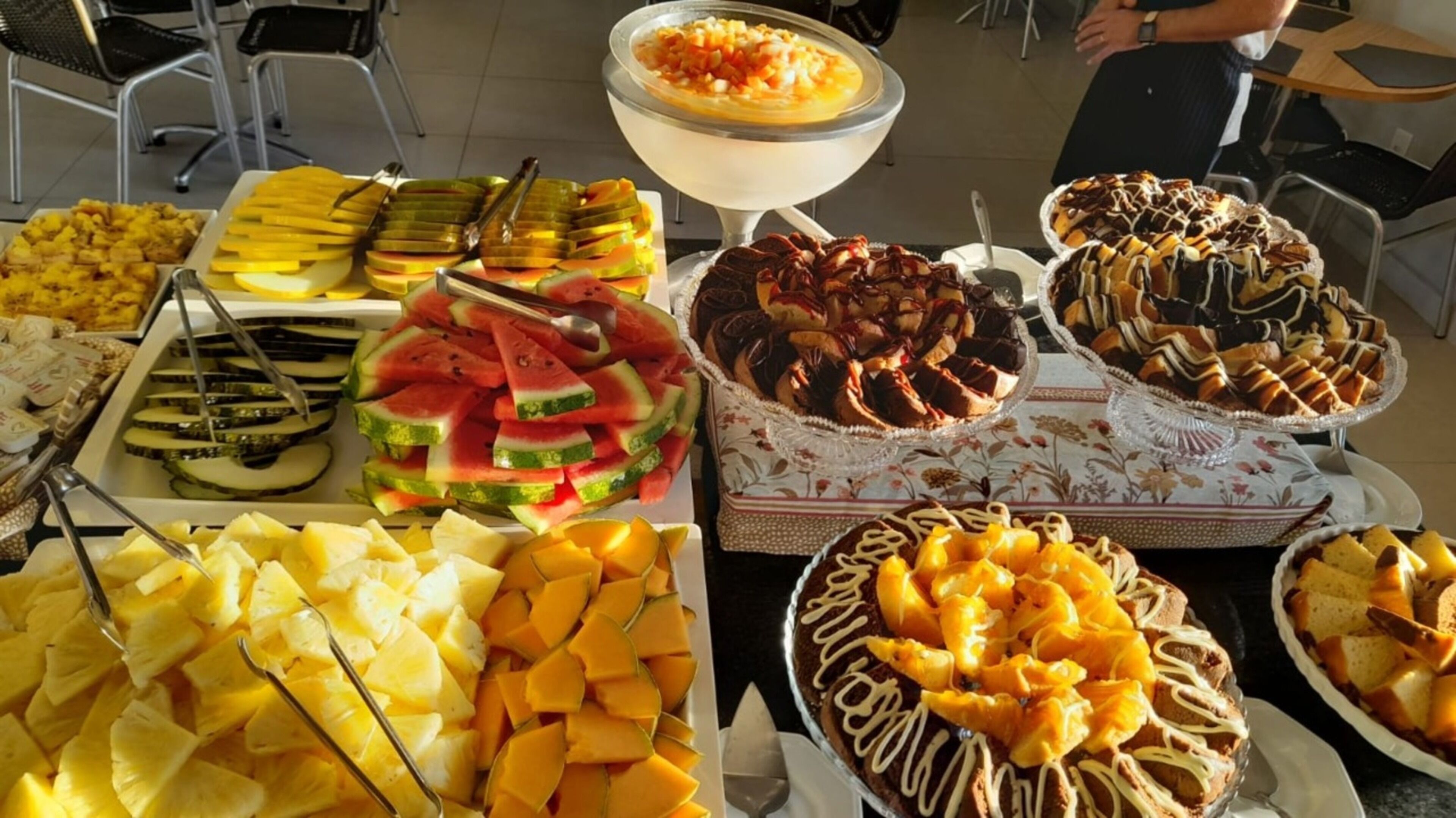 Un bufé con diversas frutas, postres y un tazón grande de sopa.